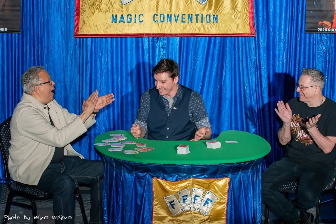 Michael Bloemeke performing close-up card magic for two laughing spectators at a magic convention close-up arena